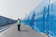 © zhu difeng - A worker in a reflective vest walks along a construction site with blue safety barriers lining the roadside