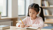 © NguyenThi - Young Asian Girl Writing In Notebook At Desk In Classroom With Books And School Supplies