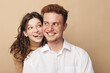 © SHOTPRIME STUDIO - Happy young couple with curly hair smiling and looking at each other. Woman playfully sticks out tongue behind man in white shirt. Concept of love, friendship, and joyful relationship.