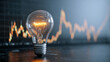 © Mikhail Vorobev - Glowing incandescent light bulb on table with blurred stock market chart in background symbolizing innovation and financial growth concept