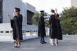 © wavebreak3 - Diverse female graduates wearing black gowns and mortarboards holding diplomas and phone on terrace