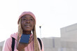 © wavebreak3 - Teen African American girl talking into phone at urban plaza in pink beanie and hoodie, backpack