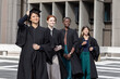 © wavebreak3 - Diverse female graduates posing on campus plaza, wearing black gowns and holding mortarboard