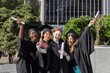 © wavebreak3 - Diverse female grads wearing gowns and caps taking selfie on campus quad with pink phone, diplomas