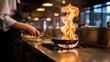 © Munawar OP - A professional chef cooking with a dramatic burst of flame in a frying pan in a restaurant kitchen.