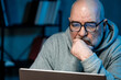 © Лиза Птицына - Concentrated professional in glasses reviewing financial metrics on computer screen after office hours. Digital business workflow concept.