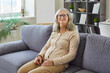 © Studio Romantic - Happy senior woman sitting on sofa in relaxing pose to enjoy carefree day with smile. Portrait of confident old lady in glasses looking at camera, relaxing on couch at home. Retirement concept