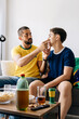 © kleberpicui - Brazilian father and teenage son watching football match together at home celebrating exciting moments. Family bonding through sports entertainment sharing emotion, support and generational connection