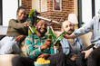 © DC Studio - African american and caucasian friends seated on couch, clinking beer bottles and socializing in cozy brick wall apartment. Happy multiethnic group enjoying casual weekend at home.