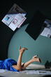 © Pixel-Shot - Young woman in high heels with many newspapers lying on floor near blue wall, closeup