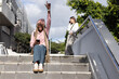 © wavebreak3 - Diverse women sitting on concrete stairway at campus, holding smartphone and notebook nearby