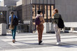 © wavebreak3 - Three women walking across university plaza, talking and gesturing with backpacks and beanie