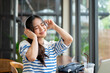 © bongkarn - Asian woman closing eyes enjoying the music in headphones while sitting at table by window in cafe.