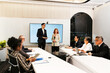 © artitwpd - Professionals in a modern conference room deliver a presentation to colleagues, with laptops and tablets around a long table and a large display