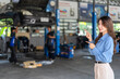 © Art_Photo - Smiling asian business woman owner pointing fingers at auto repair shop background, Female manager presenting car mechanic service, Promotion, advertisement and automotive industry concept
