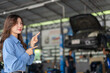 © Art_Photo - Smiling asian business woman owner pointing fingers at auto repair shop background, Female manager presenting car mechanic service, Promotion, advertisement and automotive industry concept
