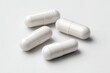 © abdulhamid - Close-up of four white capsule pills on a white surface, with slight shadows