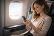 © thodonal - Young woman using smartphone while enjoying flight experience