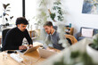© Studio Marmellata - Two men collaborate on laptops at a wooden desk in a bright, modern office space with plants.