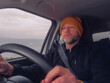 © mark_gusev - Male driver in his 40s or 50s in dark clothes and yellow hat. Man with grey beard behind driving wheel, Transport and tourism.