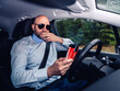© mark_gusev - Bald man with grey beard is a car driver. Stylish male in light blue shirt, dark sun glasses and looking at a smart phone. Modern technology addiction.