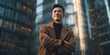 © Kowit - A confident young man in a brown coat stands with crossed arms against a backdrop of modern glass skyscrapers at dusk.