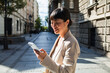 © Marko Geber - Smiling businesswoman using smartphone on a city street
