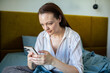 © Davor - Young woman using smartphone in bed at home