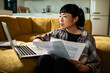 © Geber86 - Woman reviewing household bills on laptop on living room sofa