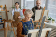 © Seventyfour - Middle aged Caucasian woman painting on canvas in art classroom, while middle aged Caucasian man and mature Caucasian woman standing at easels in background learning together
