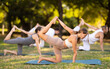 © JackF - Motivated fit young yogini engaged in outdoor group yoga session, performing stretching Vyaghrasana asana, or Kneeling Bow pose on mats in scenic summer park setting..