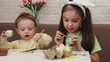 © Dilya - Happy smiling little girls and boy, kids cracking painted Easter eggs, having fun against yellow background. Concept of Easter holiday, celebration, traditions, childhood, happiness, family
