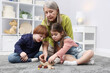 © New Africa - Nanny and cute little kids playing with wooden pieces on floor indoors