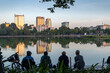© Zenstratus - Four men sit and relax by Hoan Kiem Lake in Hanoi, Vietnam, enjoying the sunset and the reflections of the city skyline on the water. They are taking in the view.