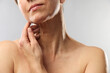 © New Africa - Woman touching her neck on light grey background, closeup