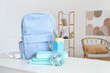 © Pixel-Shot - Backpack with stationery and books on table in room