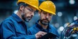 © NovaVision - Two male engineers in hard hats collaborating on a tablet in a factory setting