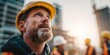 © NovaVision - Experienced construction worker in yellow hard hat looking up at building site with hope