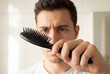 © Meow Creations - Young man holding black hairbrush full of fallen hair with concern
