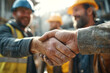 © EricMiguel - Two construction workers exchanging a firm, dirty - handed handshake in foreground with bearded colleagues in hard hats and safety vest blurred behind