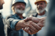 © EricMiguel - Close - up of mature bearded construction workers in hard hats exchanging a firm handshake — weathered hands, plaid shirt, warm backlight