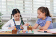 © Ekkasit A Siam - Asian girl and caucasian girl elementary classmates sharing colorful crayons during classroom art lesson representing creativity teamwork collaboration friendship childhood cooperative learning
