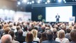 © Iuliia - Audience watching male speaker on stage at a large conference or seminar. Business presentation event for professional networking and education.