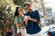 © Westend61 - Smiling couple sitting on a bench outdoors using smartphone in city