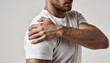 © Ipramana - Man in White T-Shirt with Hand on Shoulder Facing Right in Gray Background Showing Discomfort