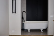 © TrueFrame Collective - Vintage clawfoot bathtub standing in modern bathroom with black wall and tiled floor, no people visible, minimalist interior design emphasizing clean lines and functional layout