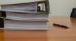 © ravikanth - Stack of business documents on desk with pen, representing paperwork management, compliance documentation and corporate record keeping.