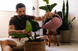 © kleberpicui - Adult man watering indoor plants in a cozy apartment living room, showing daily plant care routine, home wellbeing and sustainable urban lifestyle.