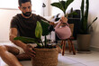 © kleberpicui - Adult man watering indoor plants in a cozy apartment living room, showing daily plant care routine, home wellbeing and sustainable urban lifestyle.