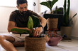 © kleberpicui - Adult man adjusting soil while repotting a houseplant indoors, representing plant maintenance, home gardening and sustainable lifestyle habits.